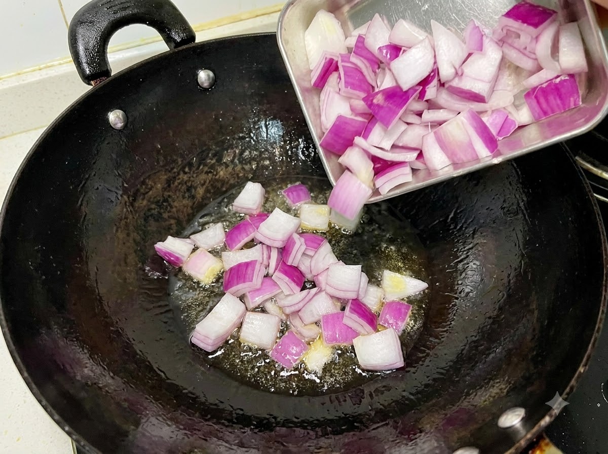 Cebolla roja picada sofriéndose en un wok negro con aceite.