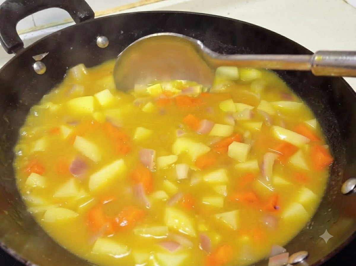 Un cucharón removiendo una salsa de curry amarilla, espesa y rica, con patatas y zanahorias en un wok.