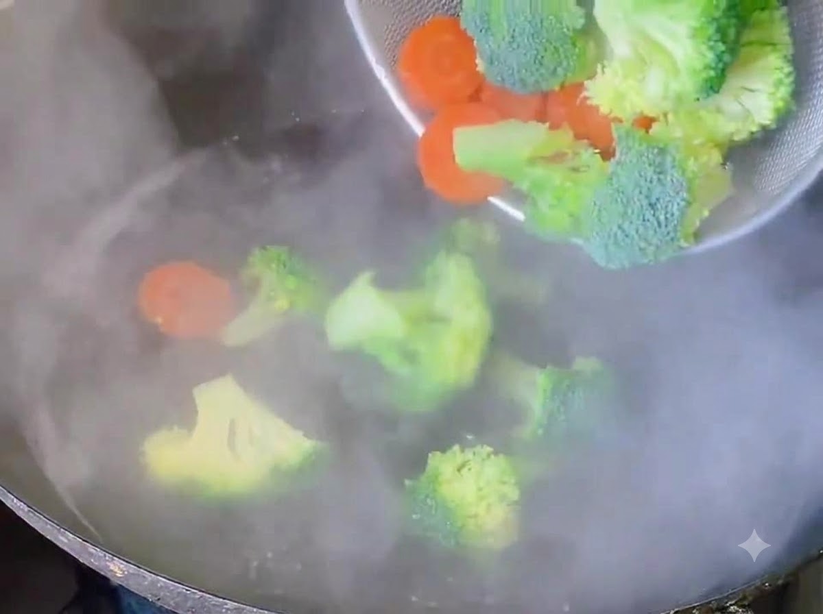 Arbolitos de brócoli y rodajas de zanahoria siendo blanqueados en agua hirviendo.