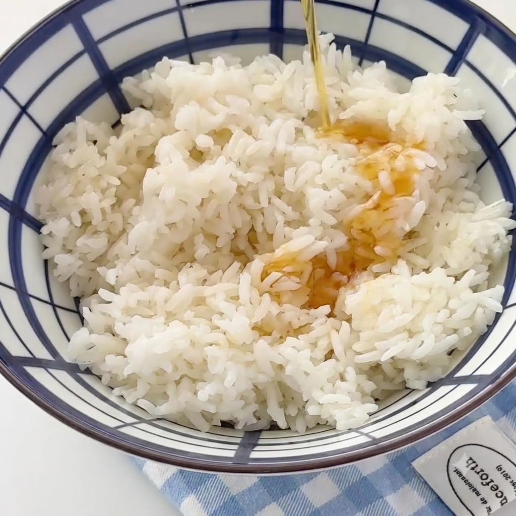 Aceite de sésamo fluyendo hacia un bol grande lleno de arroz blanco cocido.