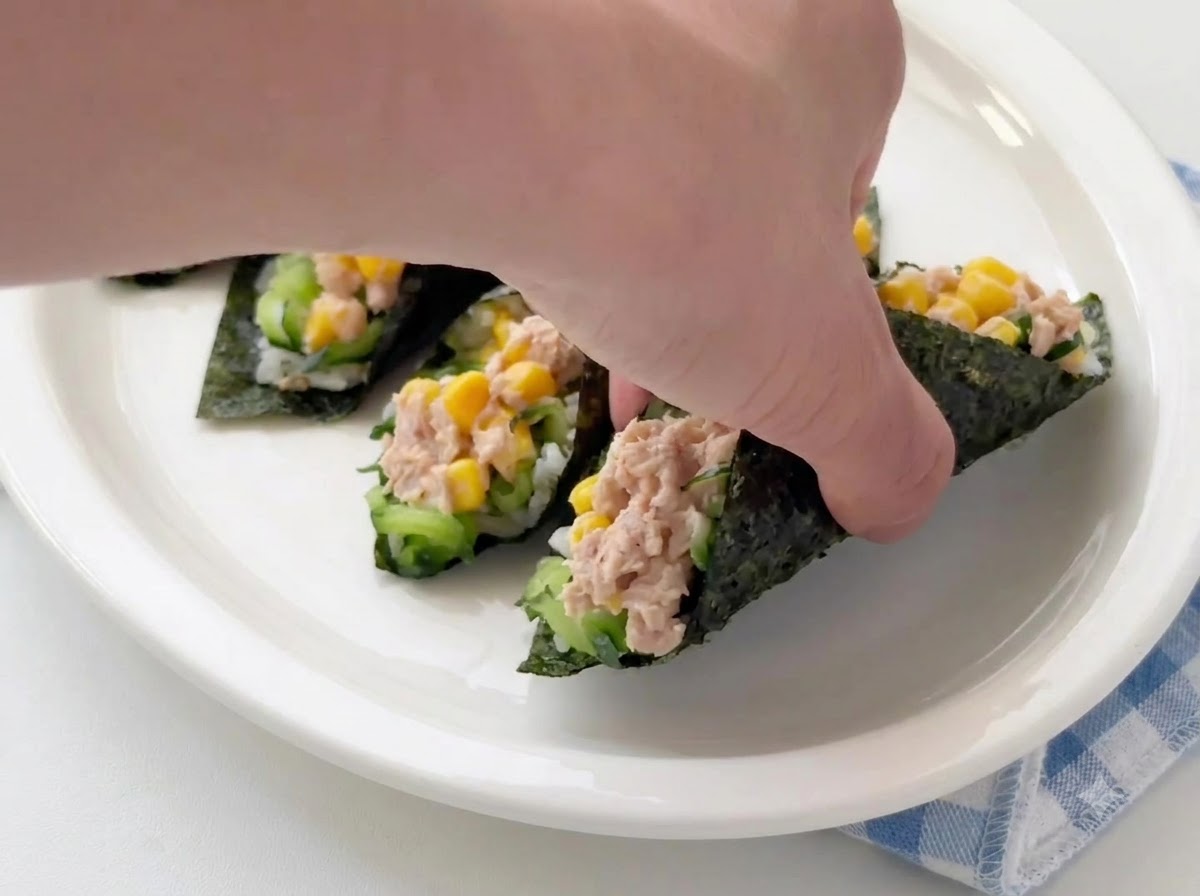 Una mano colocando o ajustando rollos de arroz con atún y alga listos en un plato de servir blanco.