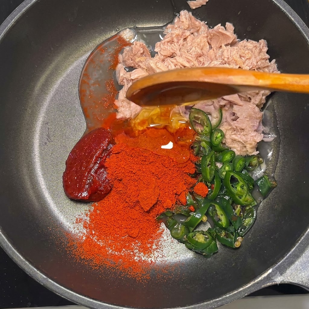 Pasta gochujang, polvo rojo gochugaru, jarabe de maíz y mayonesa reposando en la sartén sobre el atún y los chiles.