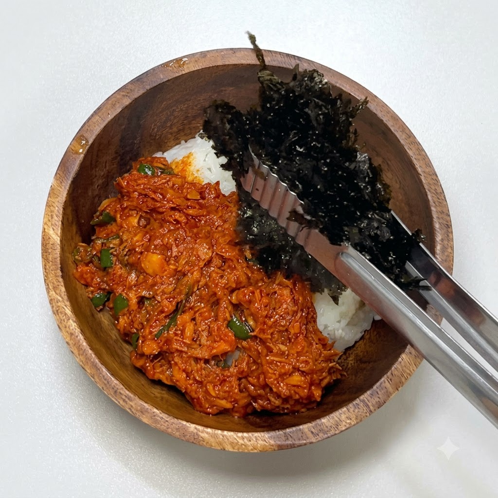 Pinzas metálicas colocando alga deshidratada triturada en el bol de madera junto al atún picante y el arroz.