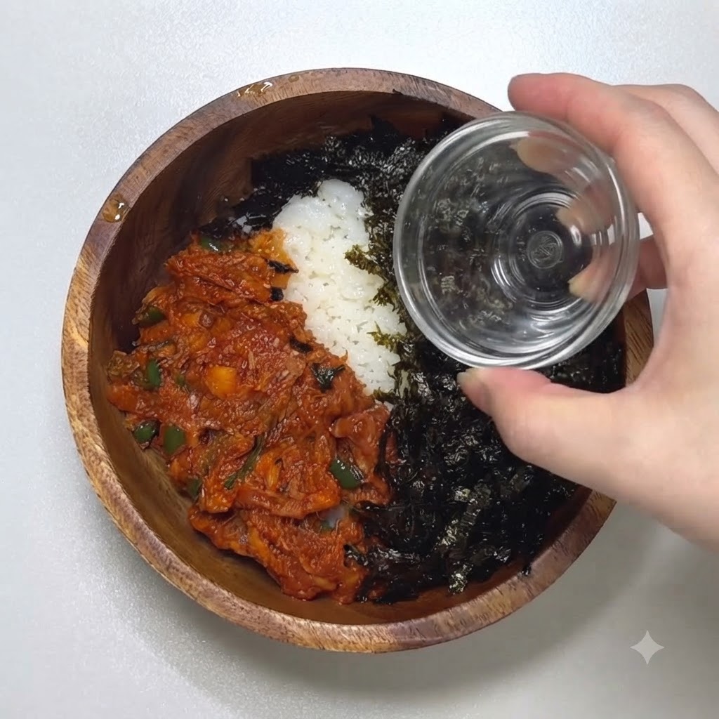 Un primer plano de una mano vertiendo semillas de sésamo tostadas desde un pequeño recipiente de vidrio sobre un bol lleno de algas sazonadas y atún picante.