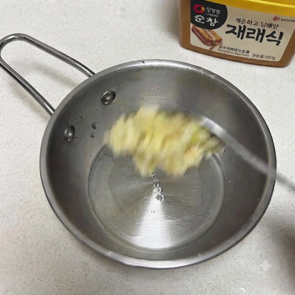 Ajo picado y semillas de sésamo siendo agregados a una sartén pequeña de acero inoxidable.