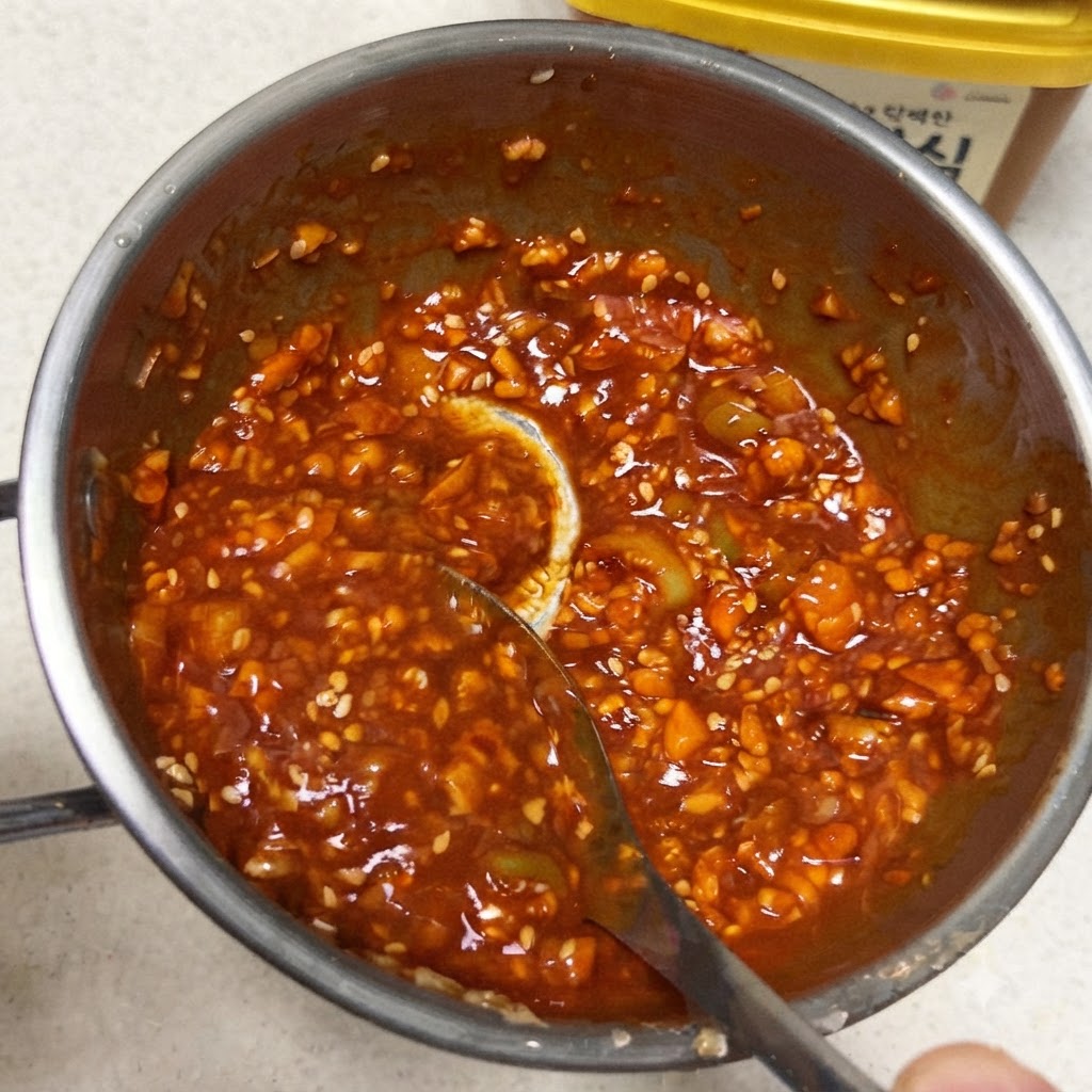 Una cuchara mezclando una salsa coreana roja espesa y vibrante dentro de una pequeña sartén de metal.