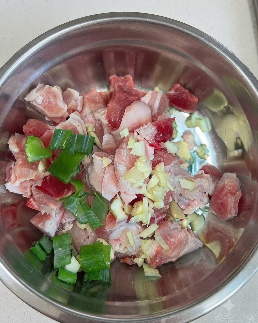 Trozos de panceta de cerdo cruda en un tazón de metal combinados con ajo, cebollas de verdeo y pasta de ají rojo.