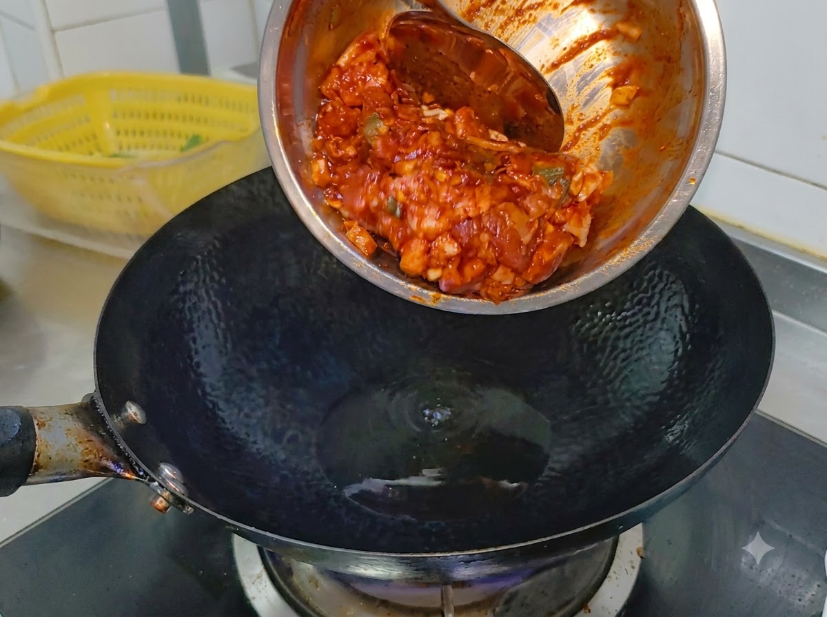 Panceta de cerdo picante marinada deslizándose desde un tazón de metal hacia un wok negro humeante que contiene aceite de cocina.