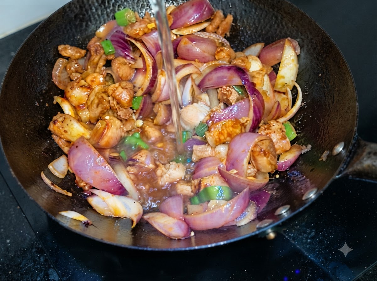 Agua vertiéndose desde arriba en un wok que contiene panceta de cerdo salteada y rodajas de cebolla morada.