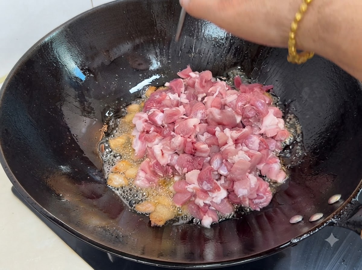 Trozos frescos de cerdo magro en cubos siendo añadidos al wok caliente con grasa derretida y especias.