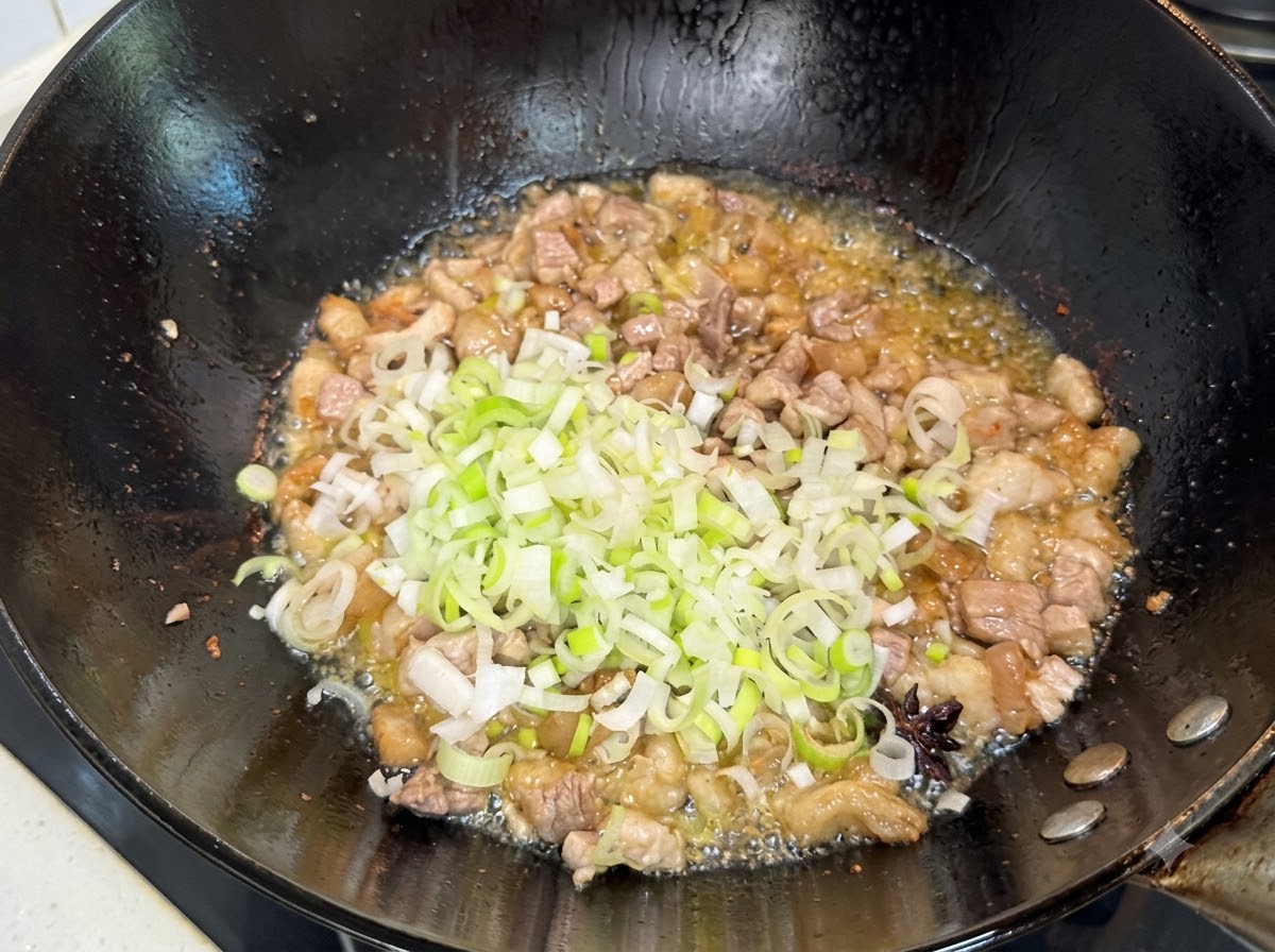 Cebollines verdes picados siendo revueltos en la mezcla de cerdo dorada en el wok.