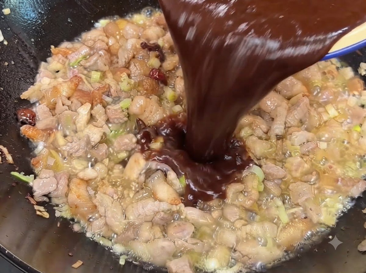 Mezcla de salsa de soja oscura y frijol dulce siendo vertida en el wok sobre el cerdo cocido.