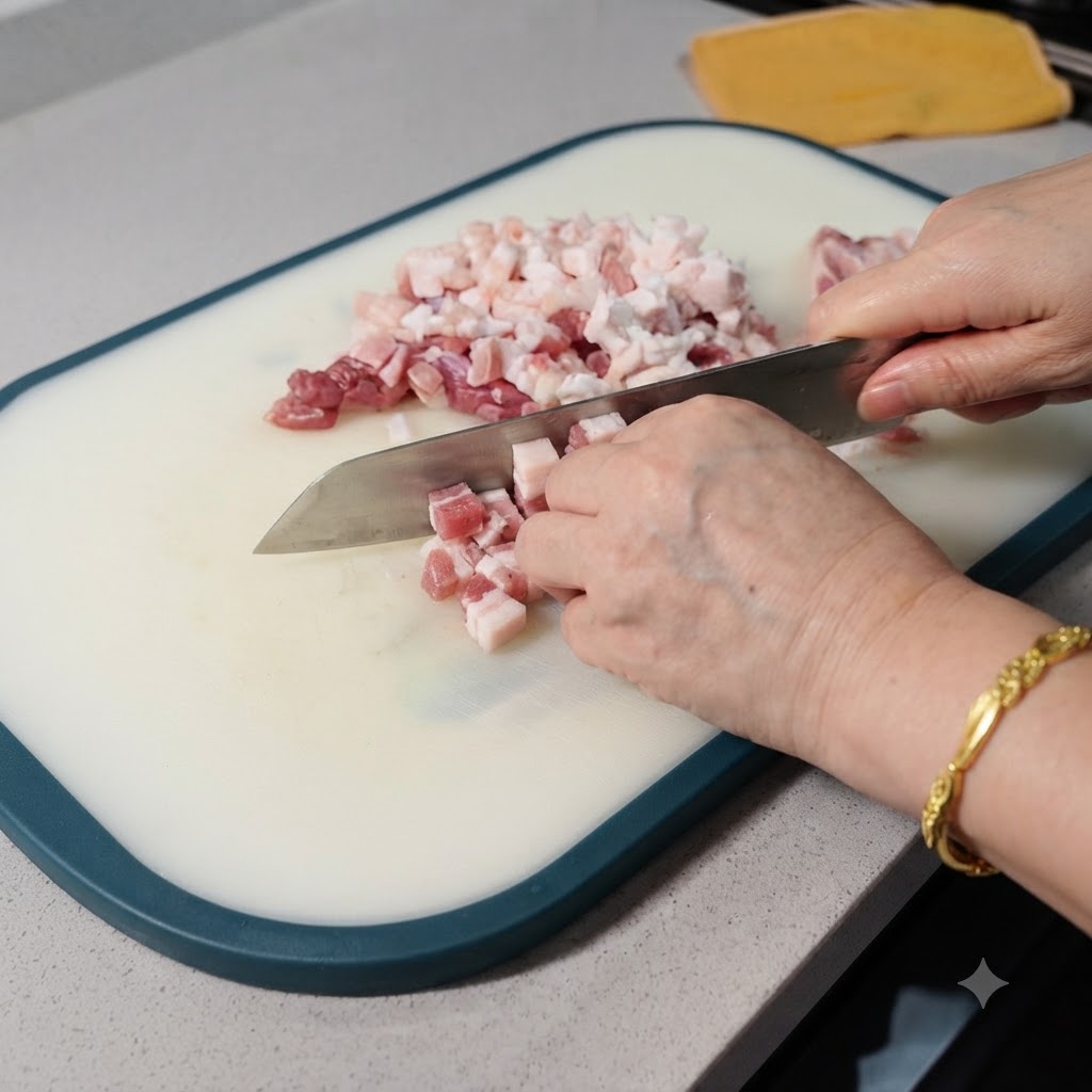 Una vista cercana de panceta de cerdo cruda siendo cortada en pequenos cubos con un cuchillo en una tabla de cortar blanca.