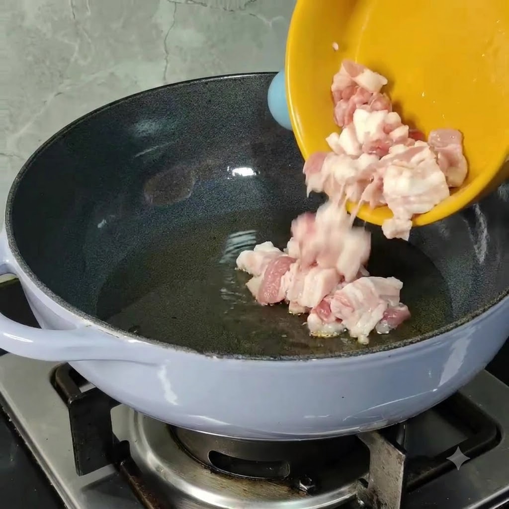 Pedazos de panceta de cerdo cruda deslizados desde un tazon amarillo hacia un sarten caliente con aceite de cocina.