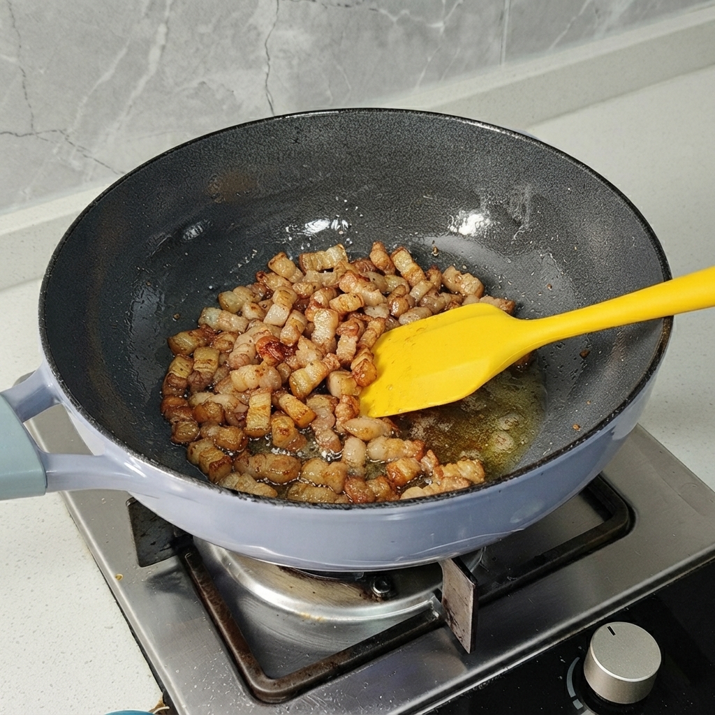 Trozos de panceta de cerdo siendo salteados en un sarten con una espátula amarilla hasta que se doren ligeramente.