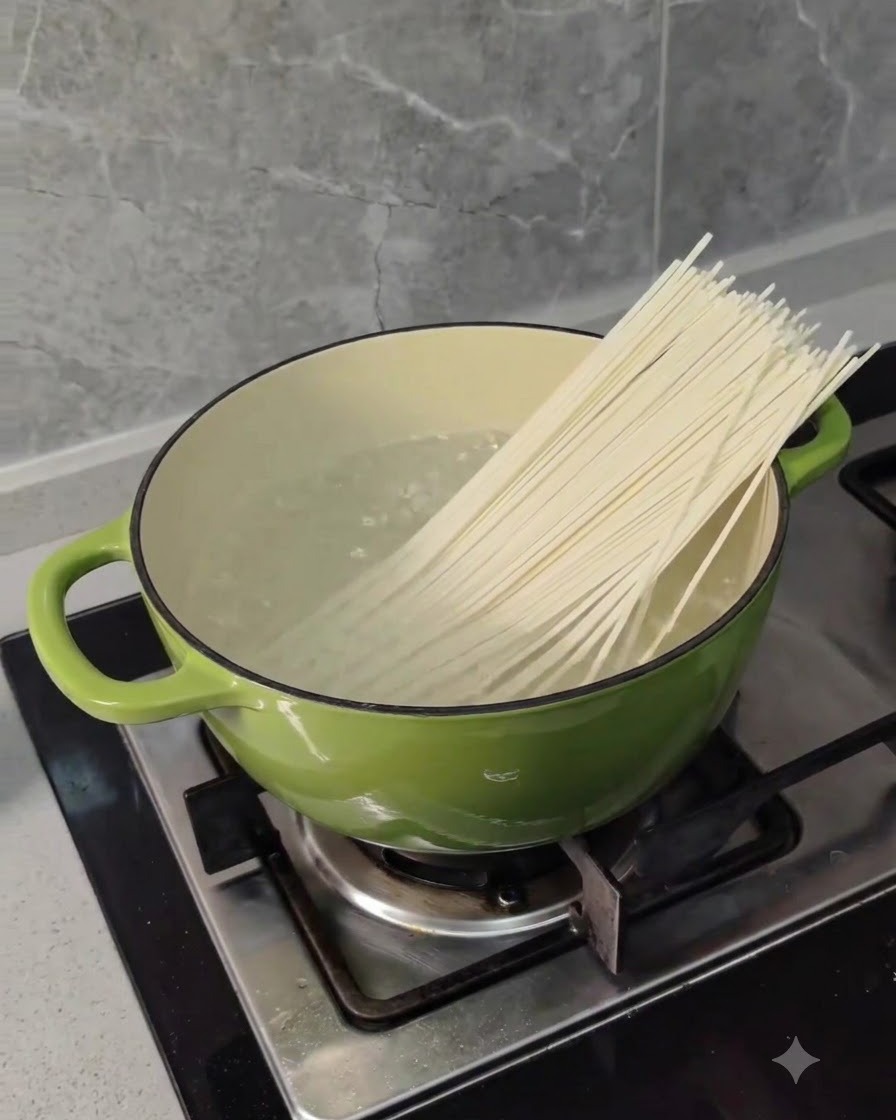 Fideos de trigo largos y secos siendo colocados en una olla verde con agua hirviendo en una estufa.