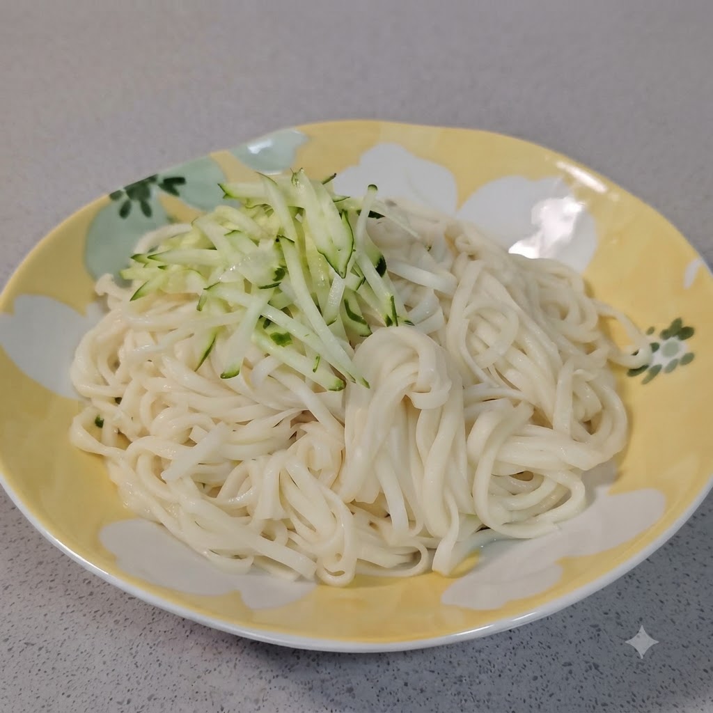Un pequeno monton de pepino rallado verde fresco siendo colocado encima de fideos blancos hervidos en un plato decorativo.