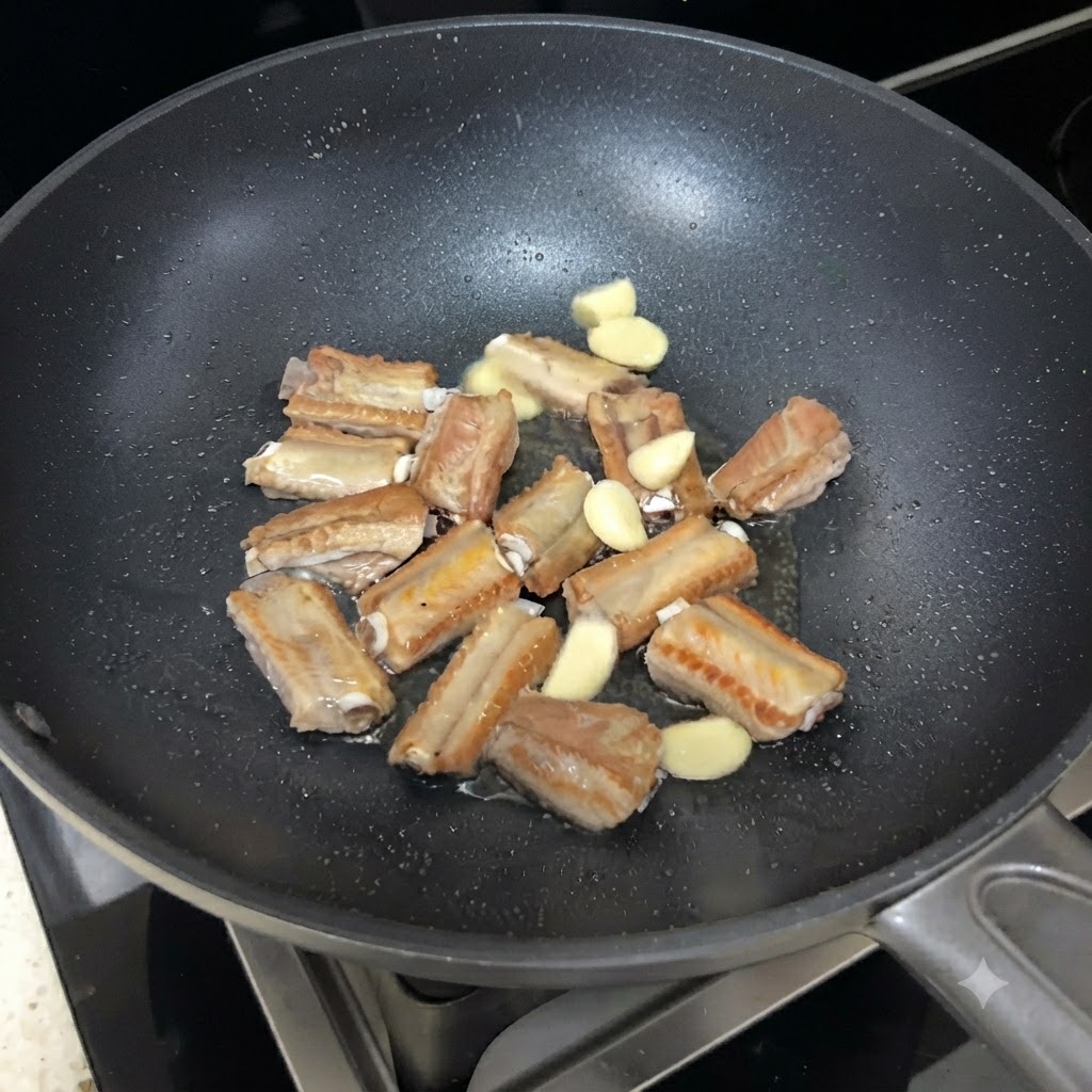 Rodajas de ajo esparcidas entre las costillas de cerdo sellándose en la sartén.