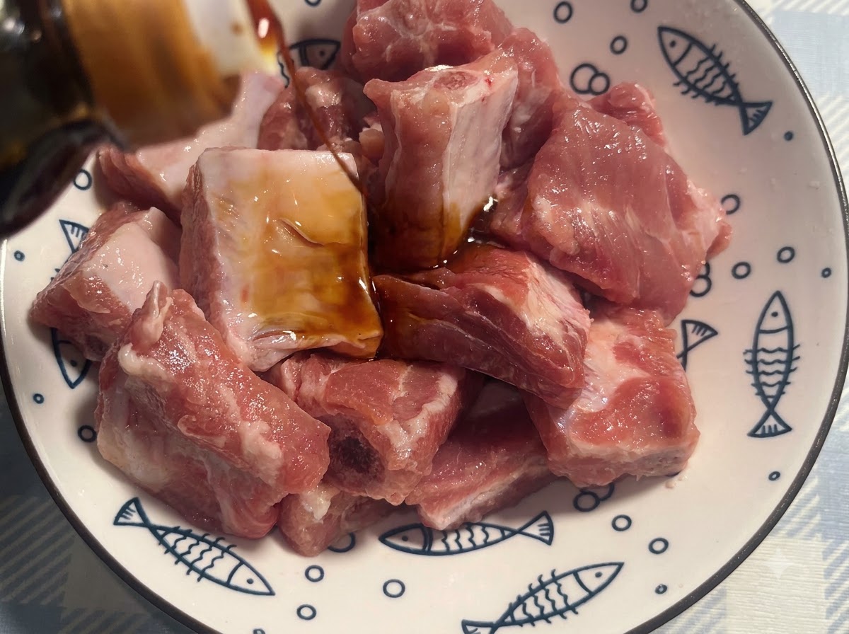 Costillas de cerdo en un bol blanco con patrón siendo sazonadas con salsa de soja oscura.