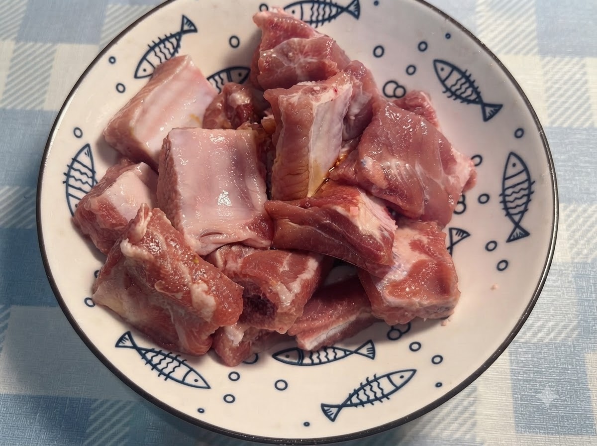 Manos con guantes removiendo y mezclando las costillas de cerdo sazonadas en un plato blanco.