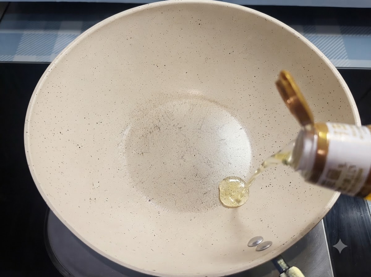 Aceite para cocinar cayendo en hilo desde una botella hacia una sartén de cerámica blanca.