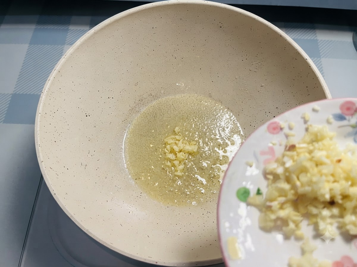 Ajo picado deslizándose desde un plato pequeño hacia la mantequilla derretida en una sartén.