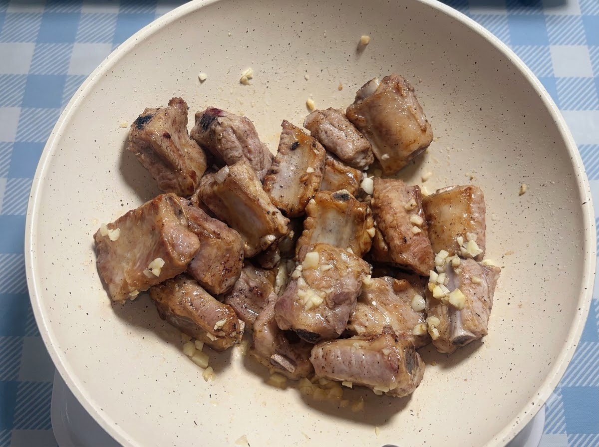 Costillas de cerdo siendo sazonadas con salsa dentro de una sartén blanca.
