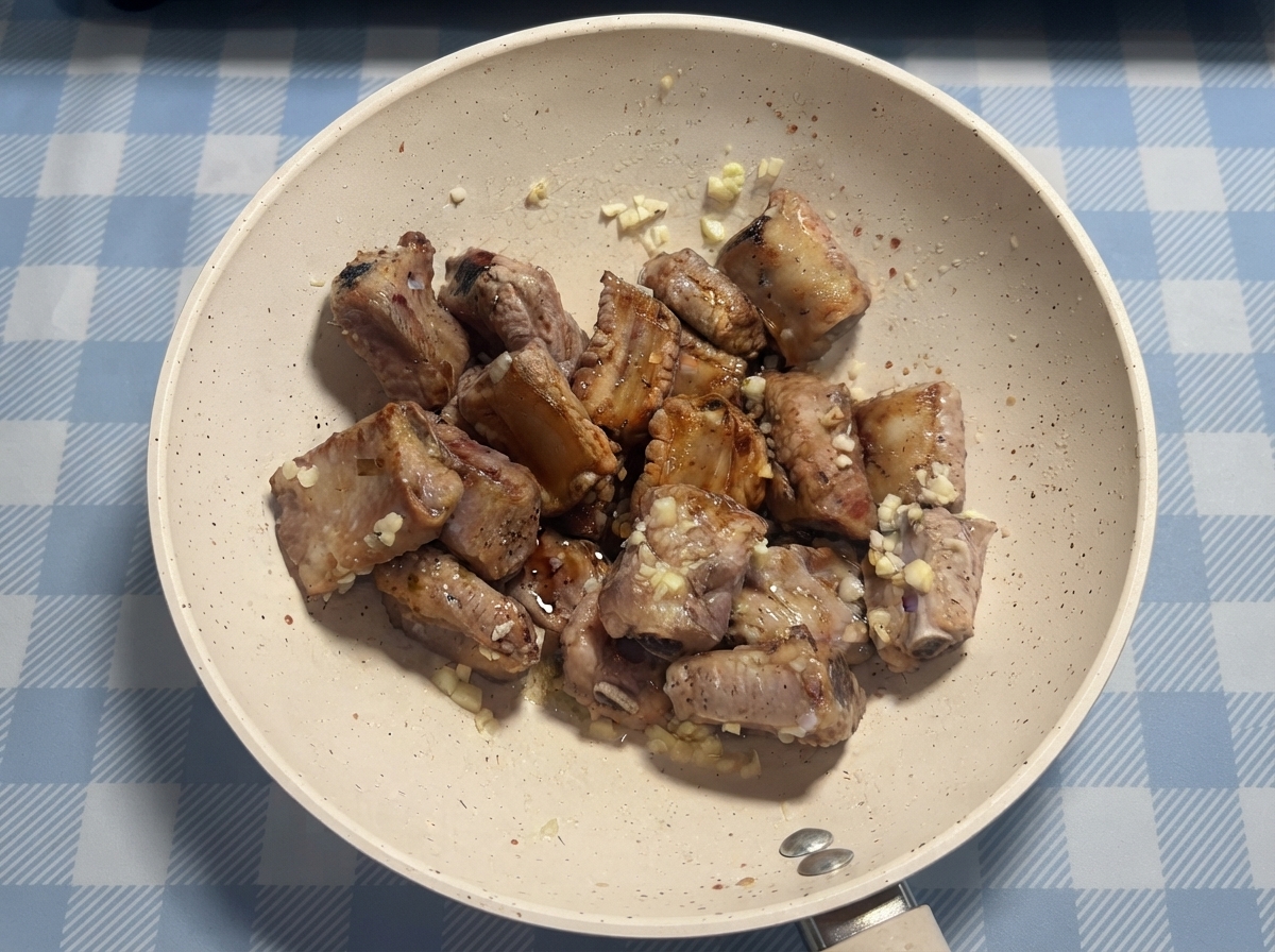 Costillas de cerdo siendo rociadas con salsa y miel en una sartén antes de la mezcla final.