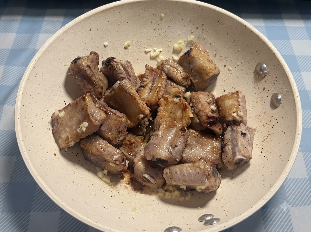 Una pizca de sal siendo espolvoreada directamente sobre las costillas de cerdo fritas.