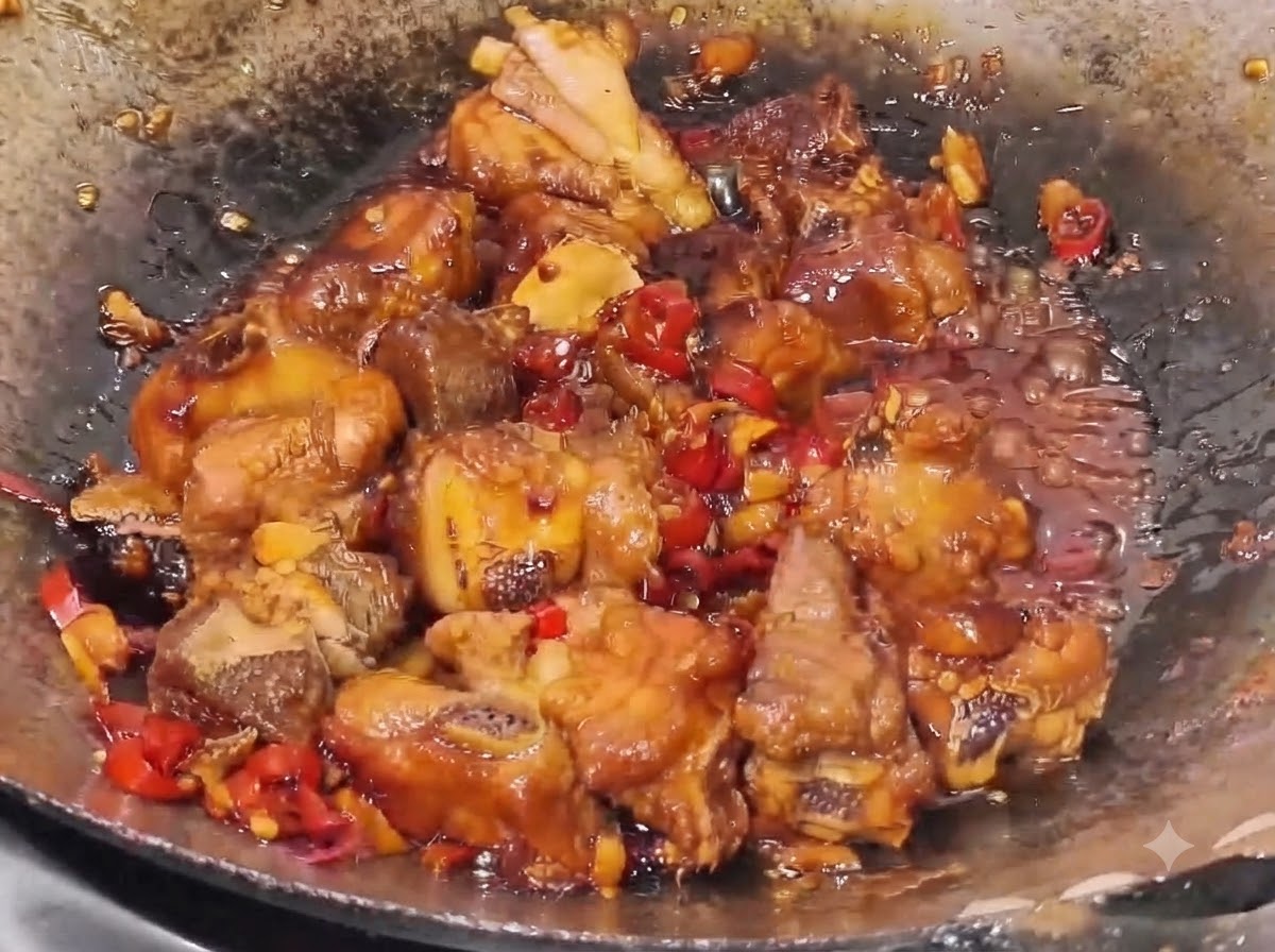 Costillas de cerdo cociéndose a fuego lento en una salsa espesa y oscura con trozos visibles de chile rojo y trozos de ajo en un wok.