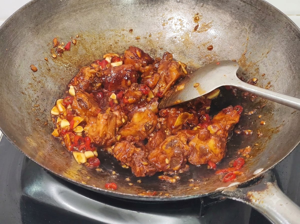 Cebollinos picados siendo mezclados en las costillas de cerdo con miel y ajo cocinadas en el wok.