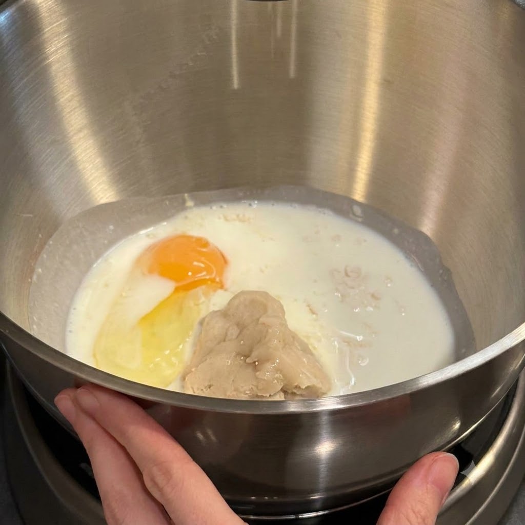 Bol de batidora que contiene harina, leche, una yema de huevo y pasta tangzhong listos para mezclar.