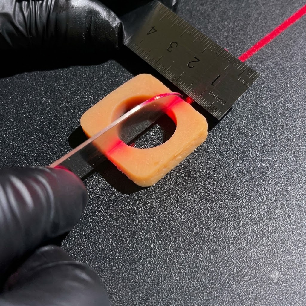 Manos con guantes usando un cuchillo afilado y una regla metálica para cortar bloques cuadrados de ingredientes bajo una línea de alineación láser roja.