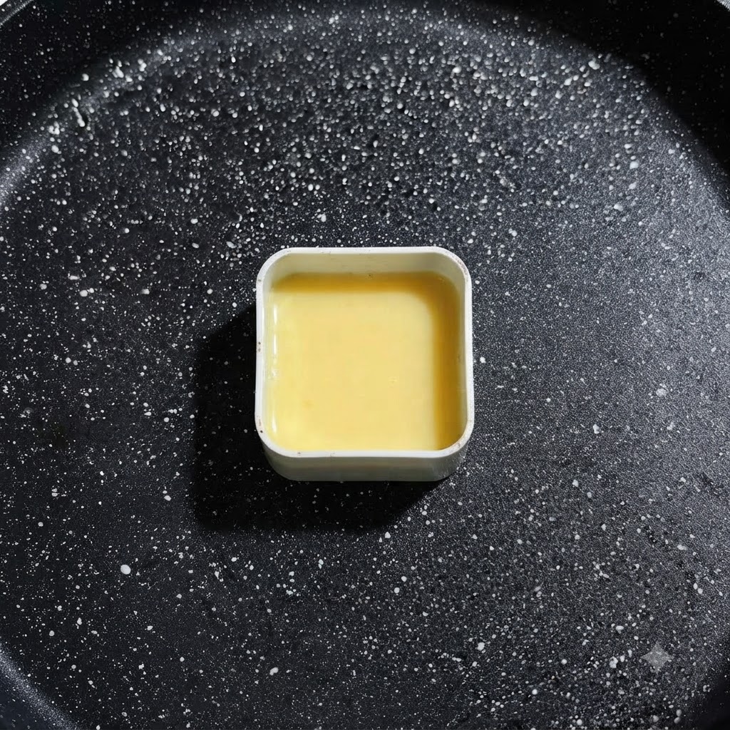 Un molde cuadrado de metal lleno de líquido de huevo amarillo reposando en la sartén de freír, listo para la colocación de ingredientes.