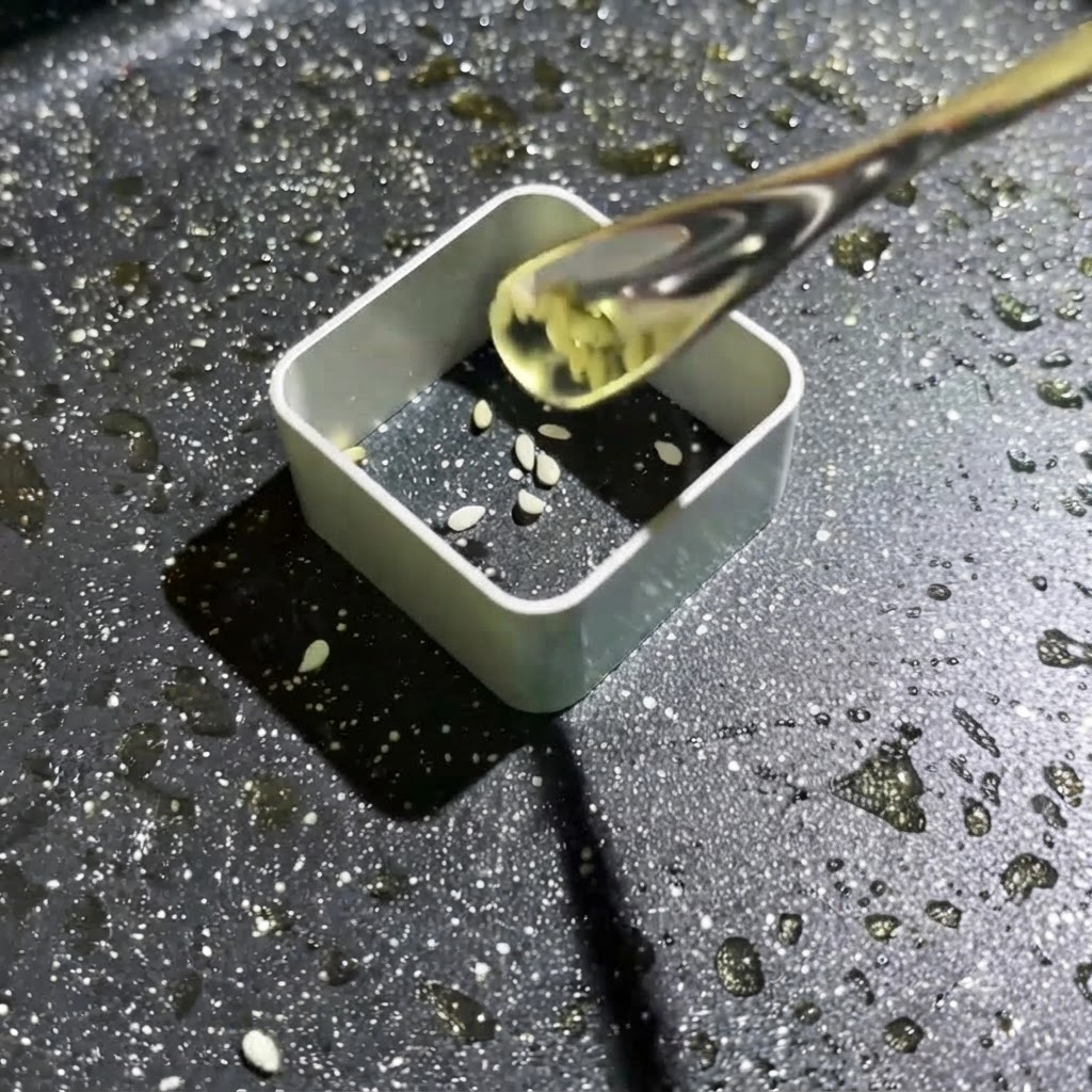 Masa con semillas de sésamo blanco siendo exprimida en un molde cuadrado.
