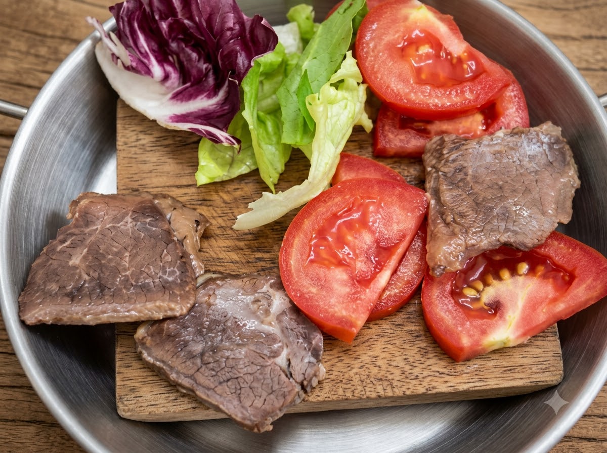 Lechuga fresca, tomates en rodajas y trozos de carne cocinada dispuestos en una pequeña tabla de madera.