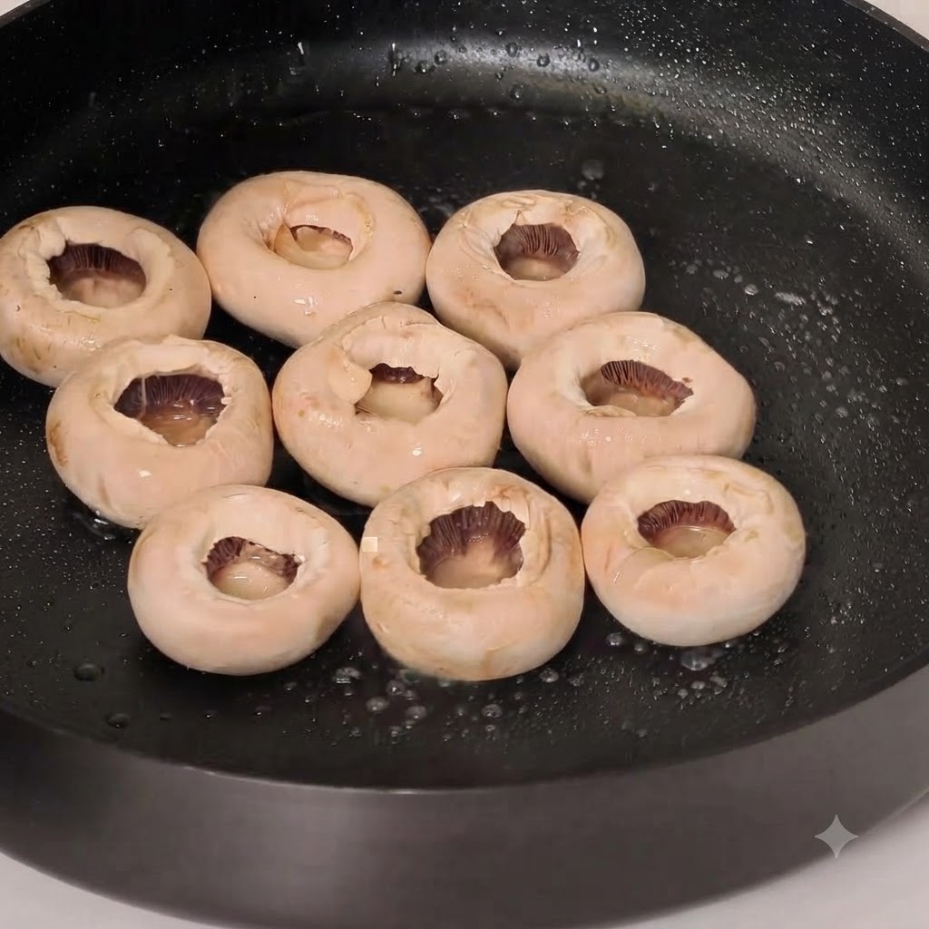 Tapas de champiñones blancos enteros friéndose en una sartén con aceite y sazonadas con pimienta.