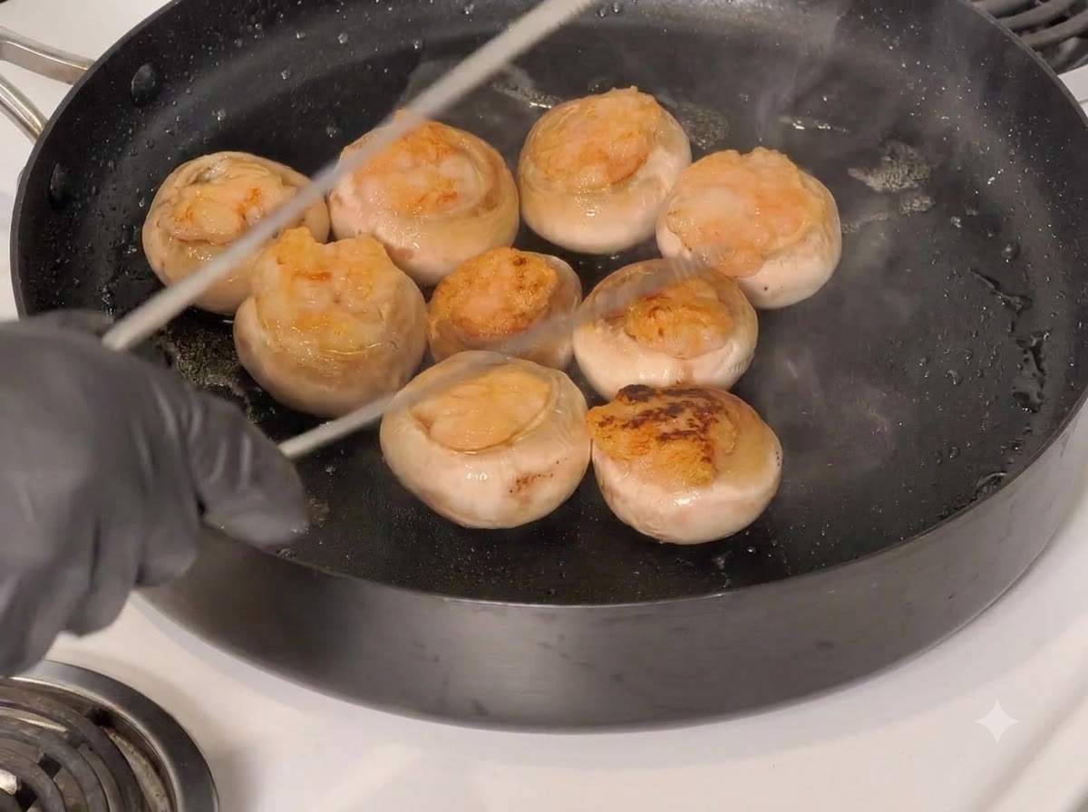 Tapas de champiñones rellenos volteándose en la sartén con unas pinzas de cocina.