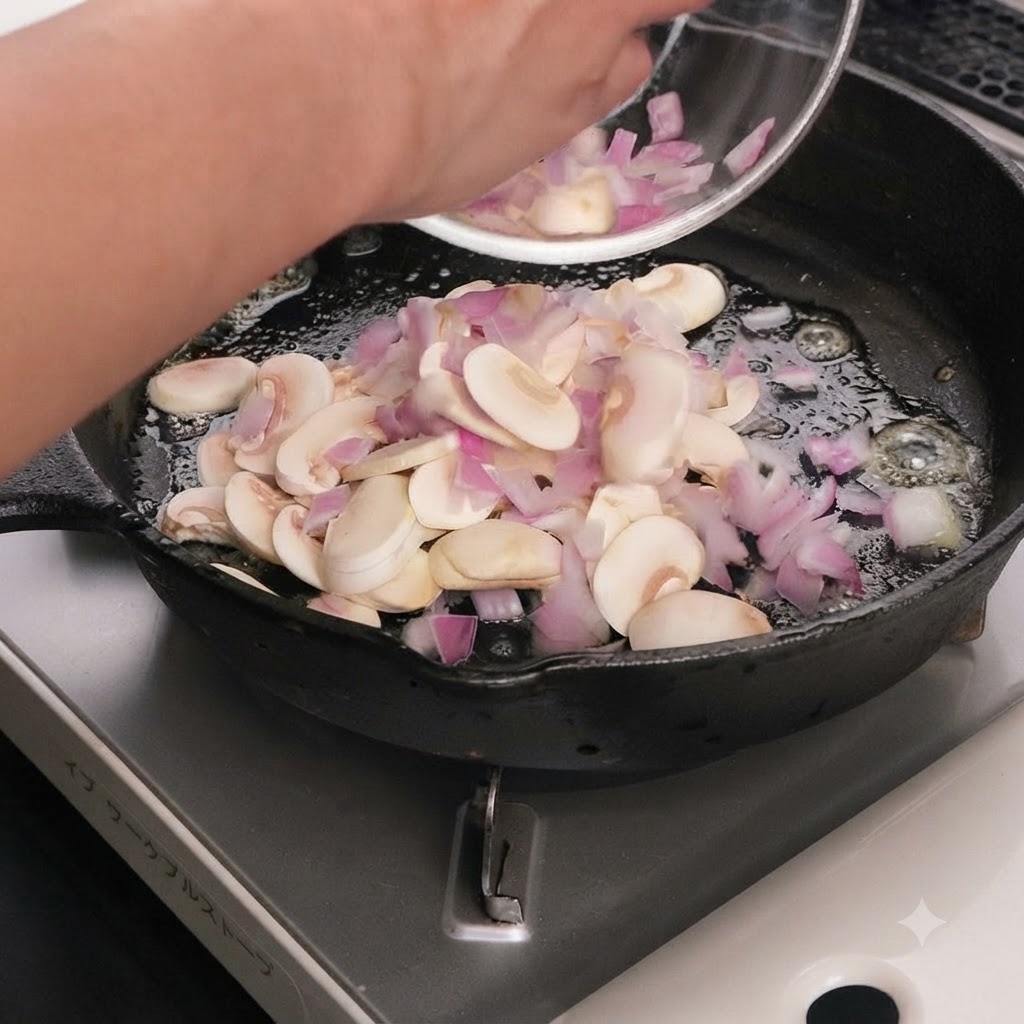 Champiñones en rodajas y cebollas moradas cociéndose en mantequilla derretida dentro de una sartén de hierro fundido.
