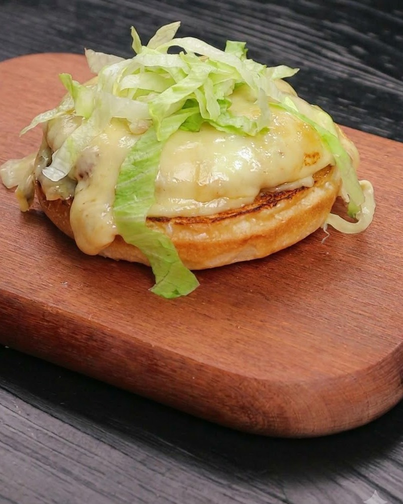 Lechuga fresca rallada amontonada ordenadamente sobre una hamburguesa de carne con queso fundido que descansa sobre una base de pan tostado.