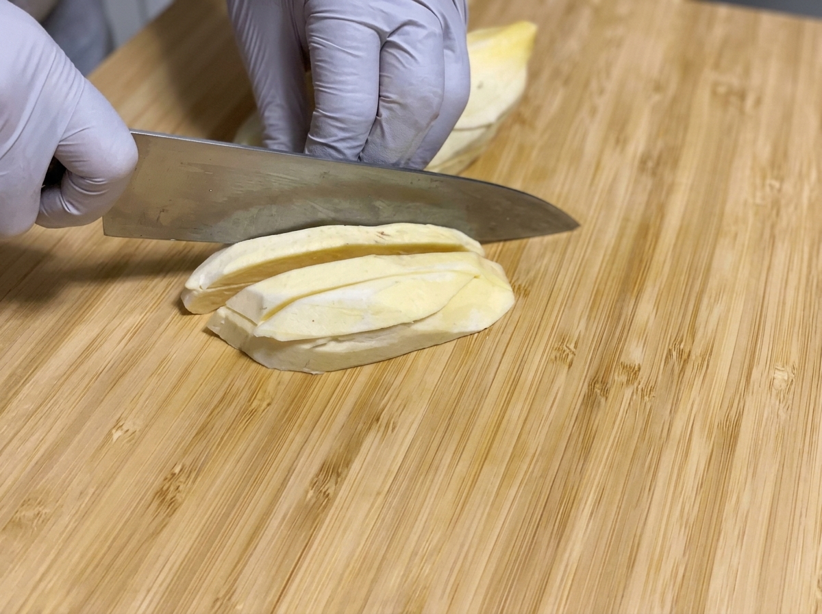 Batatas crudas peladas siendo cortadas en palitos largos con un cuchillo sobre una tabla de cortar de madera.