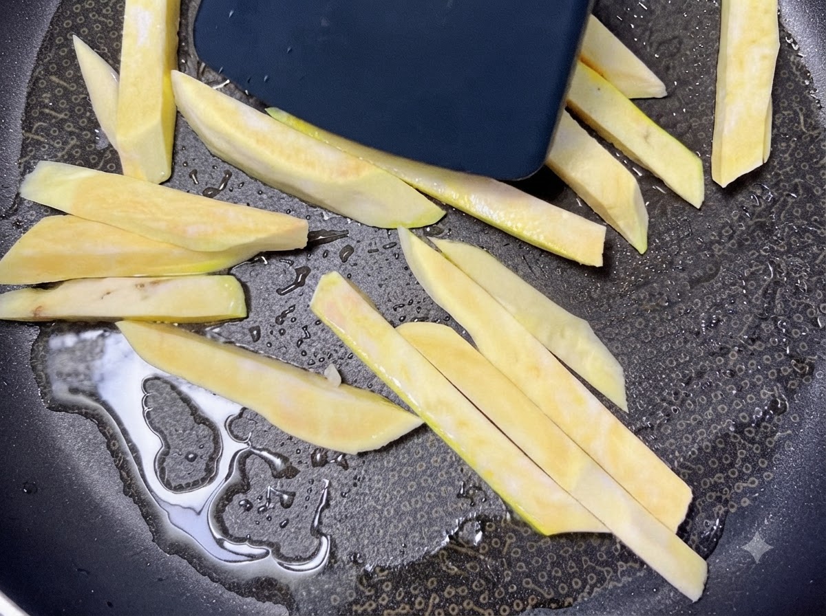Bastones de batata cruda chisporroteando en una sartén negra caliente con aceite mientras se mueven con una espátula.