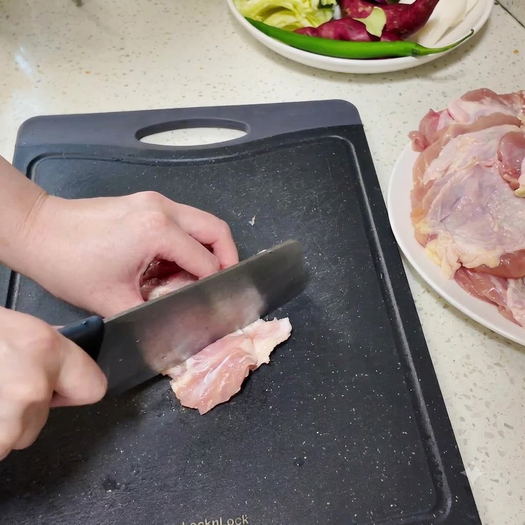 Muslos de pollo deshuesados siendo picados en trozos más pequeños sobre una tabla de cortar negra.