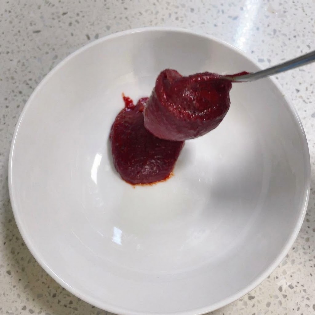 Pasta de chile coreana y otros condimentos siendo revueltos dentro de un tazón blanco.