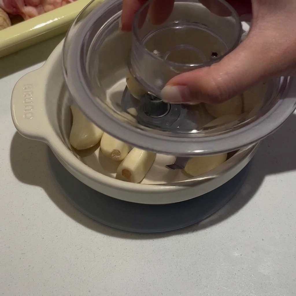 Una persona presionando la tapa de un pequeño procesador de alimentos manual lleno de dientes de ajo pelados.