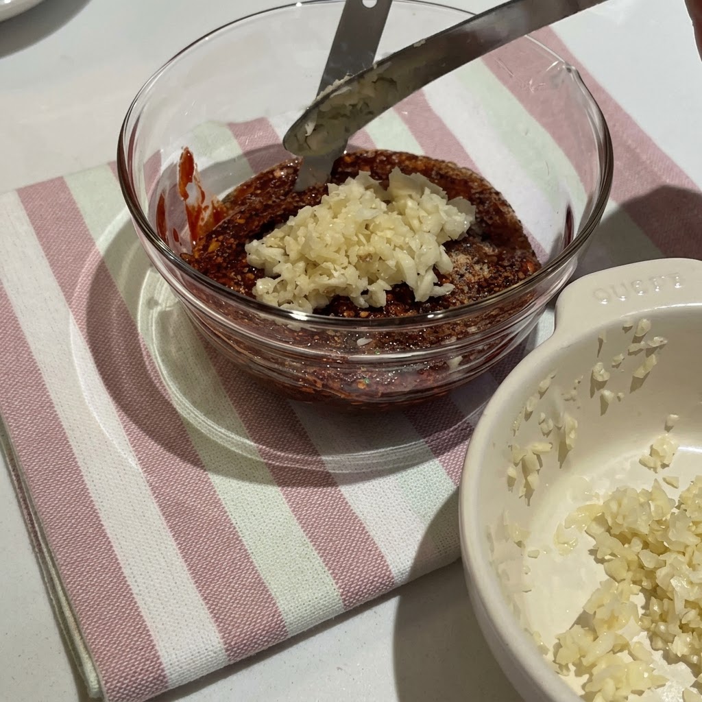 Pasta de chile coreano y varios condimentos mezclándose en un tazón de vidrio para crear una salsa roja espesa.