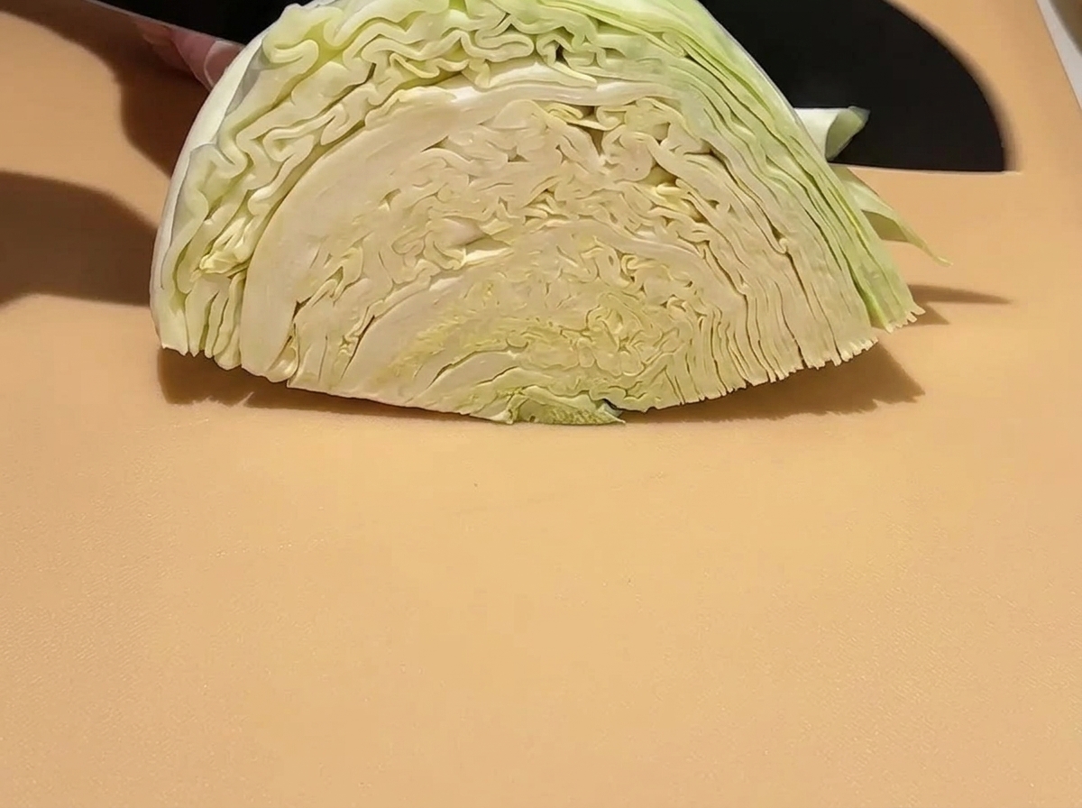 Un trozo de repollo verde crudo siendo cortado en trozos más pequeños sobre una tabla de cortar con un cuchillo.