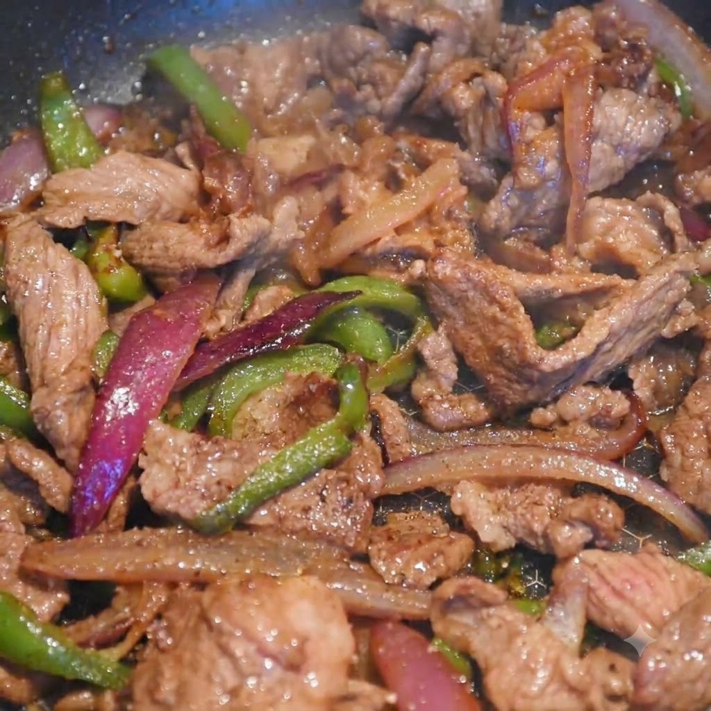Tiras de carne y verduras coloridas cocinándose juntas en una sartén mientras se añade el sazón.