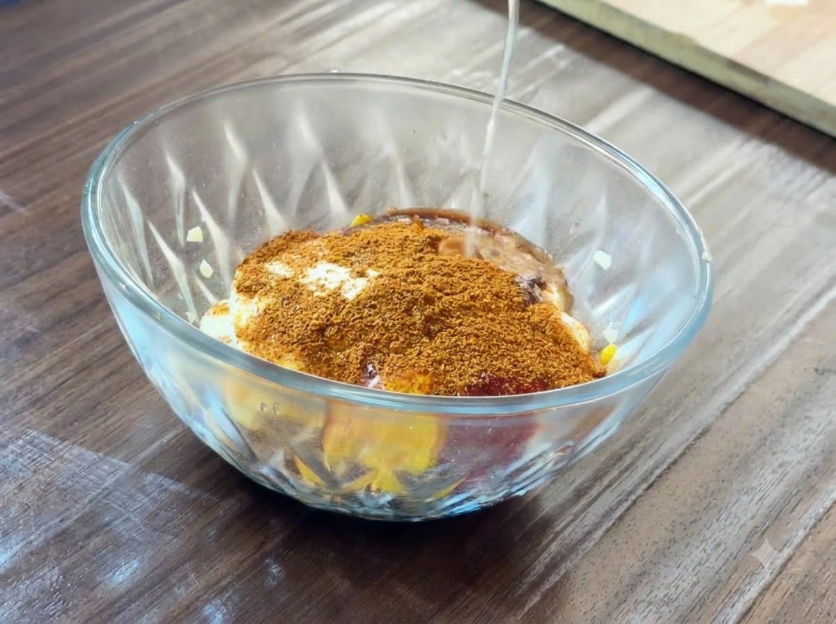 Jugo de limón fresco siendo vertido desde la mitad de un limón hacia un tazón de vidrio lleno de varios ingredientes de salsa.