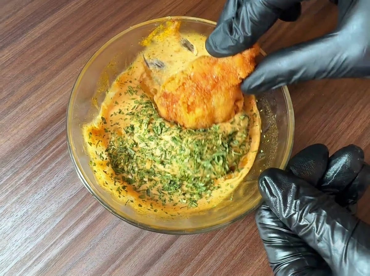Perejil recién picado siendo espolvoreado sobre un tazón de salsa para hamburguesas preparada mientras un trozo de comida frita se sumerge en ella.